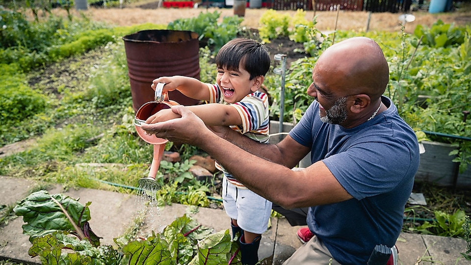 Un homme aide un enfant souriant à arroser des plantes dans un jardin