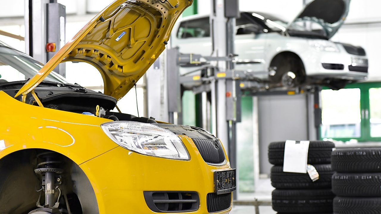 deux voitures dans un garage, une jaune et une blanche, avec le capot ouvert, et des pneus de voiture à l’arrière-plan