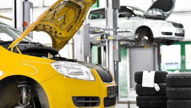 deux voitures dans un garage, une jaune et une blanche, avec le capot ouvert, et des pneus de voiture à l’arrière-plan