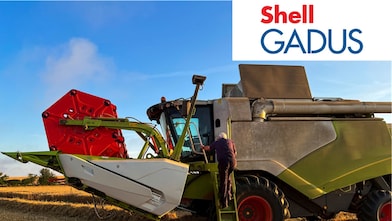 Une personne monte les marches d’une grande moissonneuse-batteuse dans un champ.