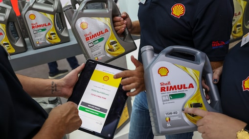 Trois personnes tenant des bidons de Shell Rimula et une tablette affichant le Shell CO₂ and Energy Tracker. En arrière-plan, des étagères remplies d'autres bidons de Shell Rimula.