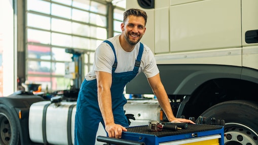 Portrait d’un mécanicien poids lourd souriant, tenant des outils, debout à côté d’un camion dans un atelier. Entretien et maintenance de véhicules poids lourds.