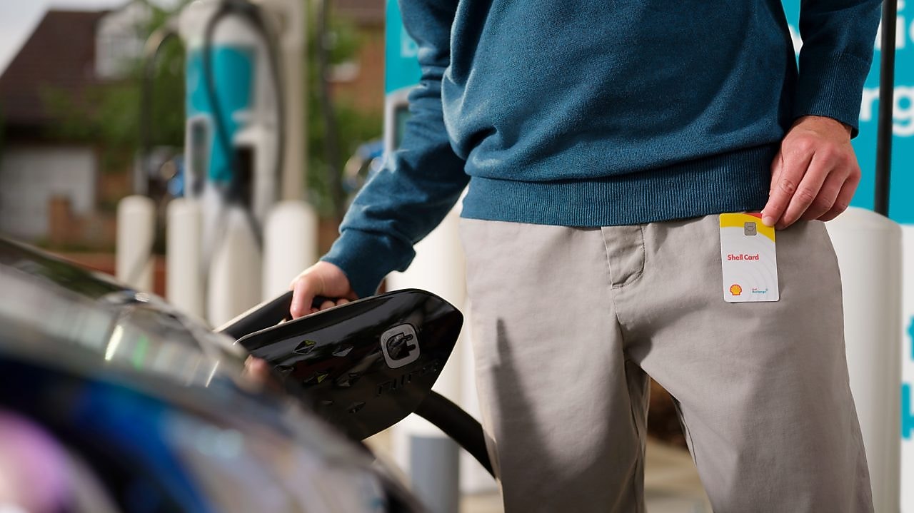 Male Shell customer holding a Shell card and recharging his vehicle on a Shell forecourt.