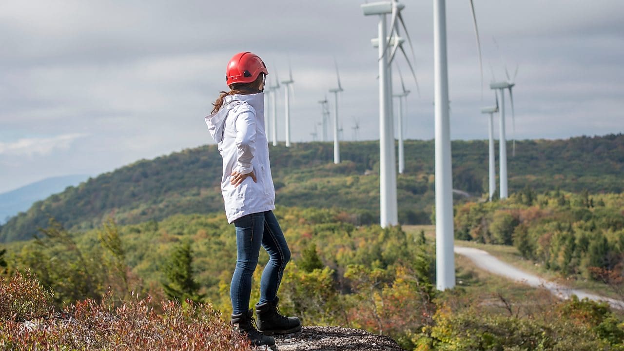 A female Shell employee standing in front of a wind turbine.
