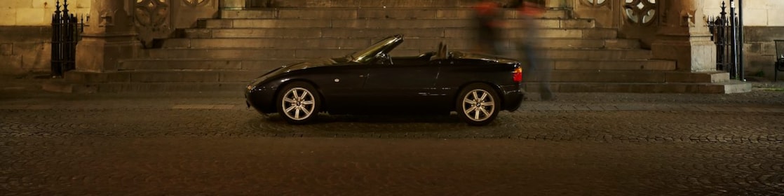 Une voiture noire garée devant une grande maison de nuit, à côté de marches en pierres