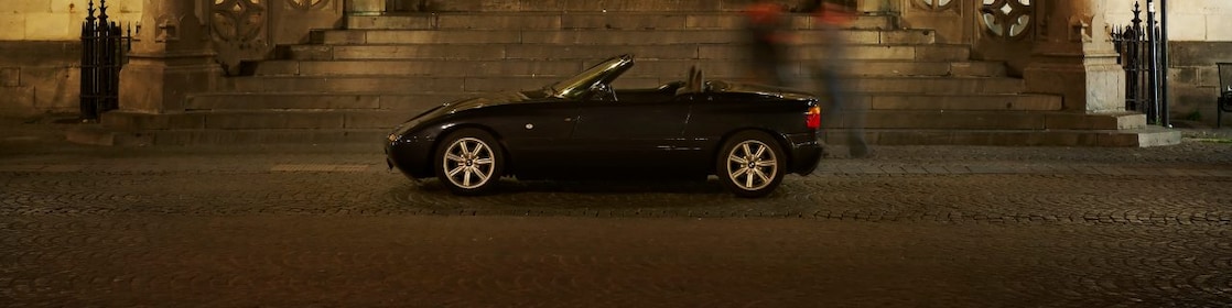 Une voiture noire garée devant une grande maison de nuit, à côté de marches en pierres