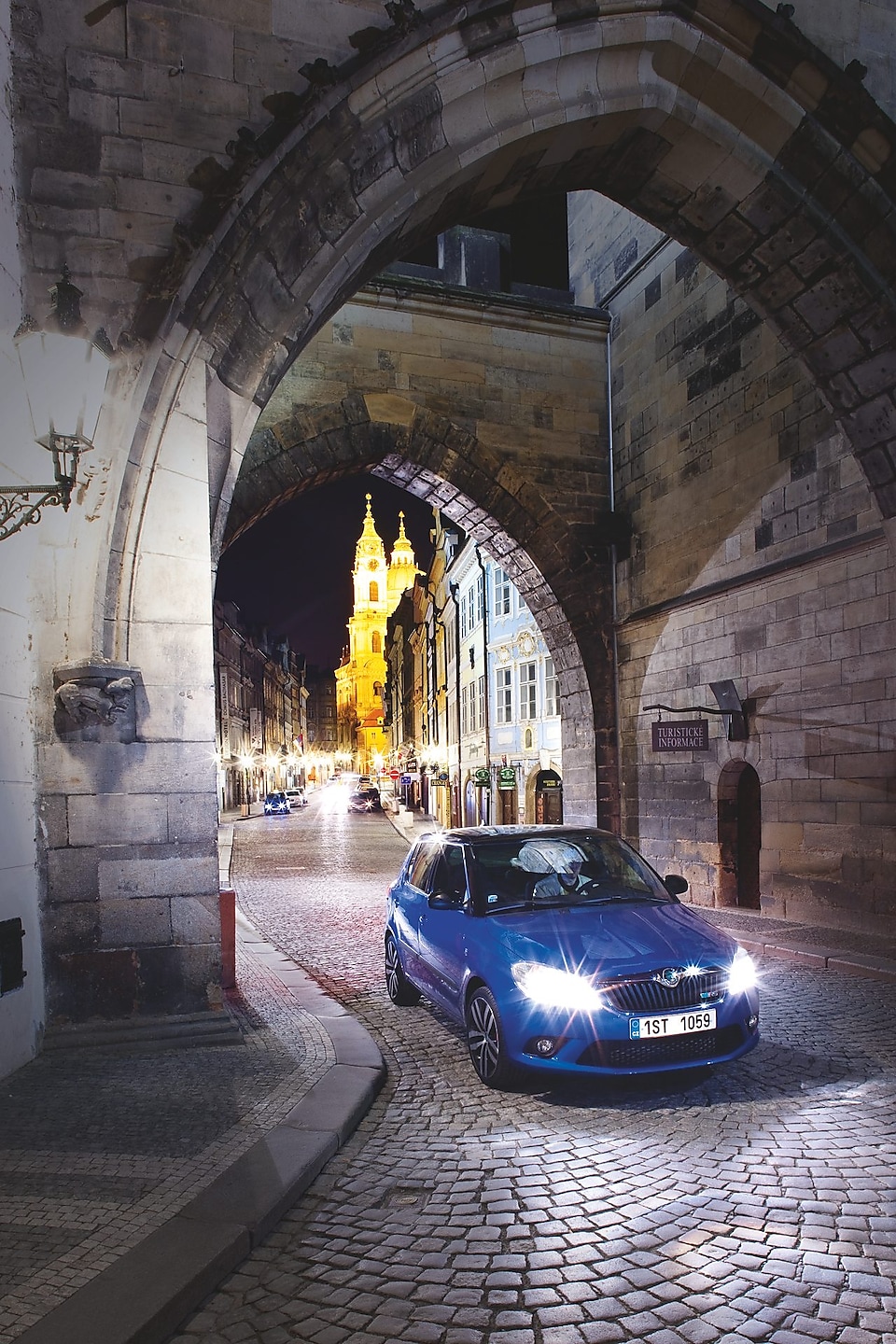 Une voiture bleue sous une arche dans une rue pavée de Prague de nuit