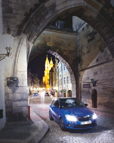 Une voiture bleue sous une arche dans une rue pavée de Prague de nuit