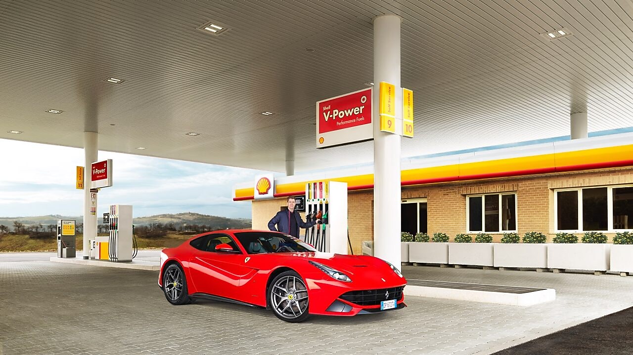 Une Ferrari rouge arrêtée à la pompe d'une station Shell avec un homme qui s'apprête à faire le plein