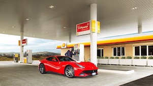 Une Ferrari rouge arrêtée à la pompe d'une station Shell avec un homme qui s'apprête à faire le plein