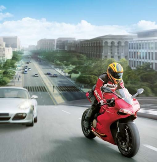 Moto rouge et motard sur une route avec des voitures et des bâtiments en arrière-plan